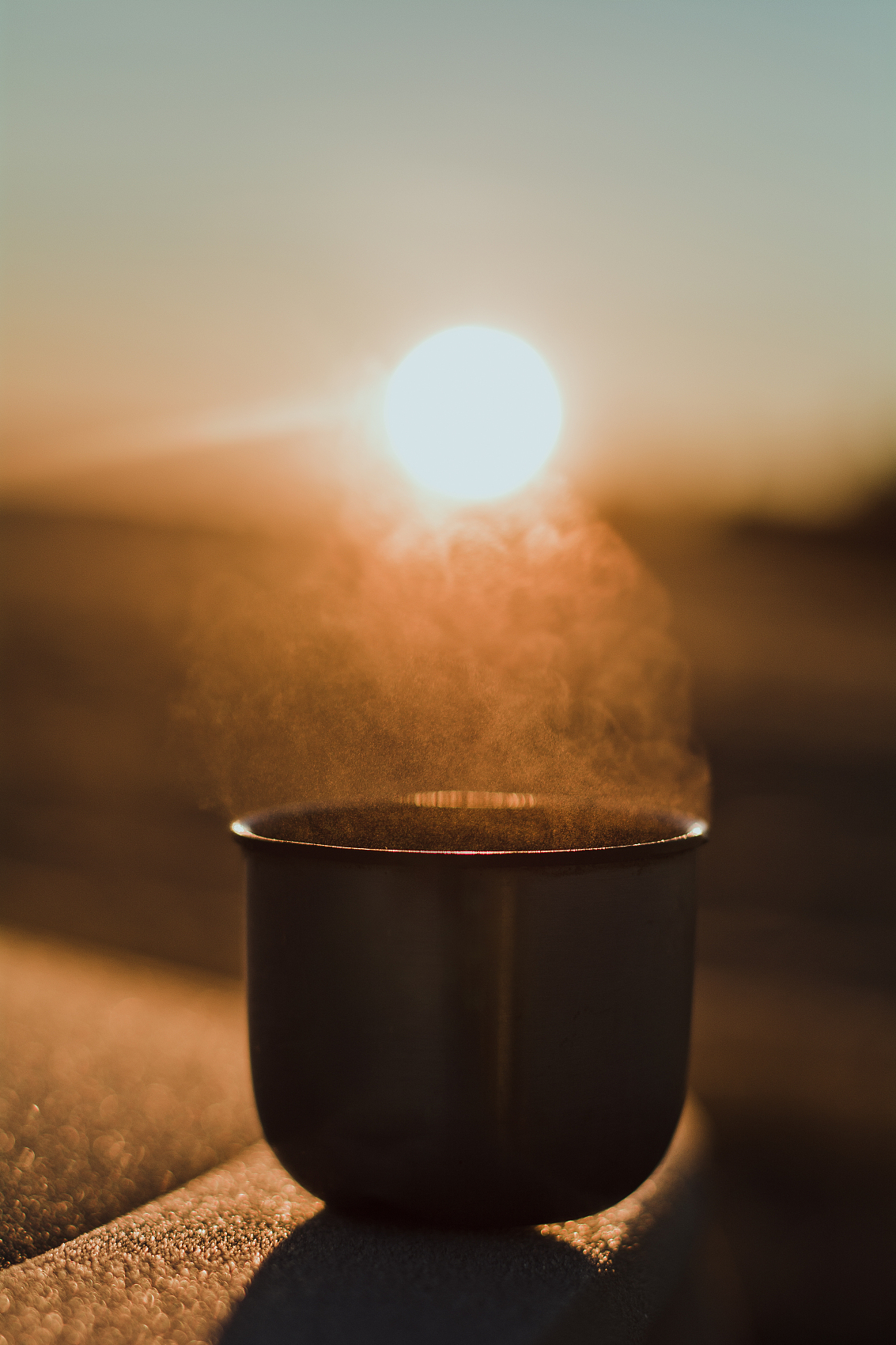 被冬天早晨的太阳照亮的热水瓶里的热茶杯的蒸汽